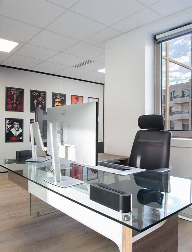 Photo du bureau de direction au siège de CEGELEM, avec son plateau en verre, son voile de fond blanc et son piètement panneau en bois walnut