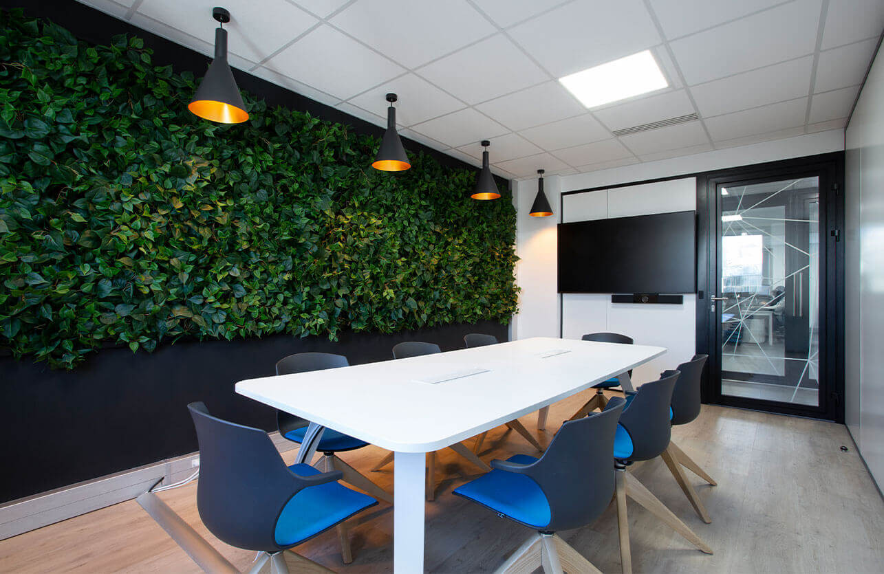 Photo d'une salle de réunion de CEGELEM avec un écran, un mur végétal, une table de réunion blanche et des chaises multicolores
