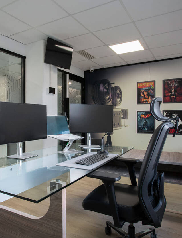 Photo du bureau de direction de CEGELEM vue du côté de l'utilisateur, avec un fauteuil en cuir noir et un bureau bi-matière avec plateau en verre et un piètement en bois